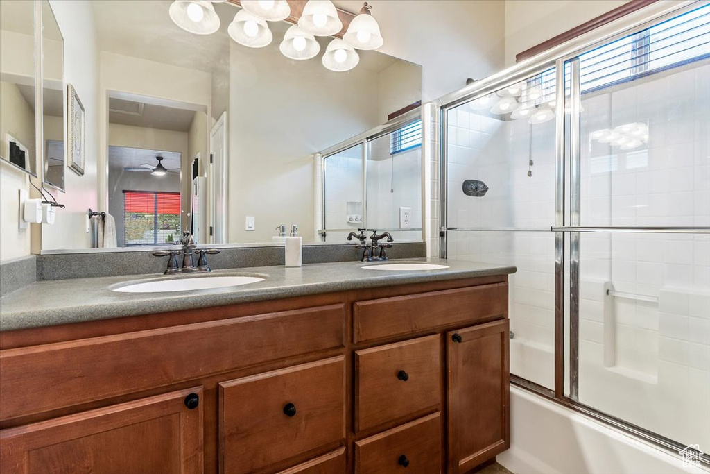 Bathroom featuring double vanity, bath / shower combo with glass door, and ceiling fan