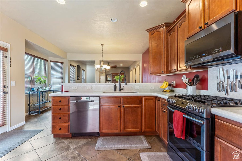 Kitchen featuring appliances with stainless steel finishes, a chandelier, a peninsula, light countertops, and brown cabinets