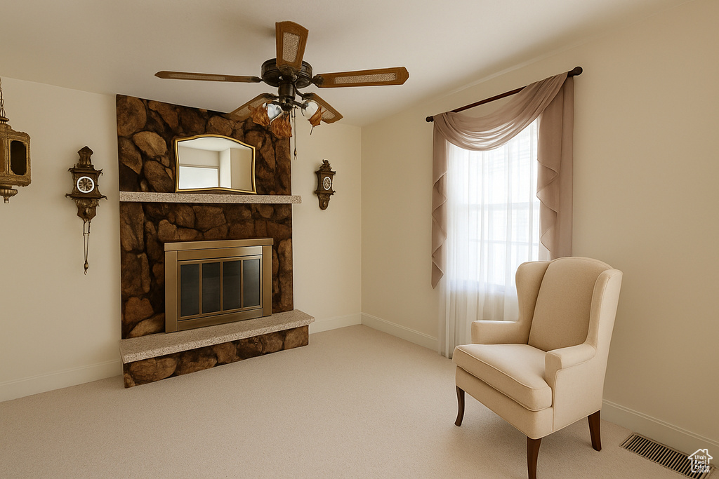 Sitting room with ceiling fan, a stone fireplace, and carpet floors