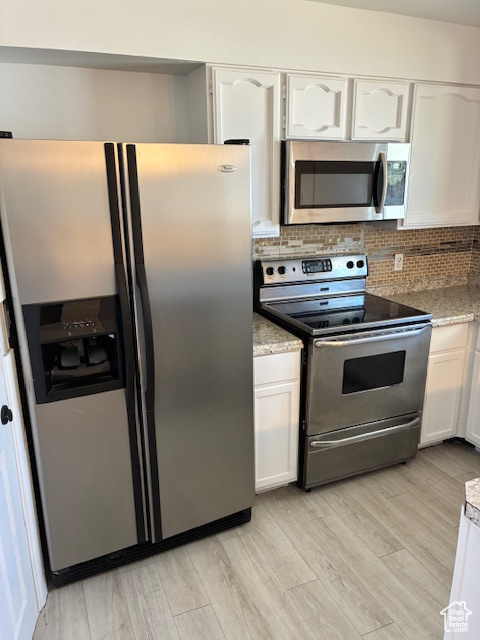 Kitchen with appliances with stainless steel finishes, white cabinets, backsplash, and light wood-style floors