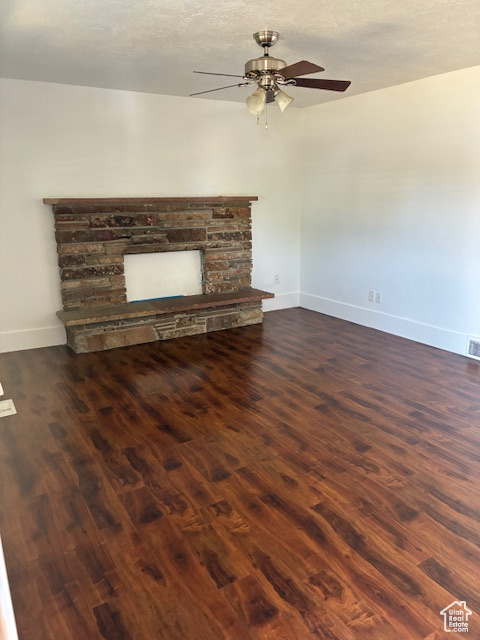 Unfurnished living room featuring wood finished floors, ceiling fan, and a stone fireplace