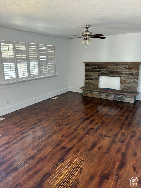 Unfurnished living room featuring ceiling fan, dark wood-style floors, a textured ceiling, and a stone fireplace