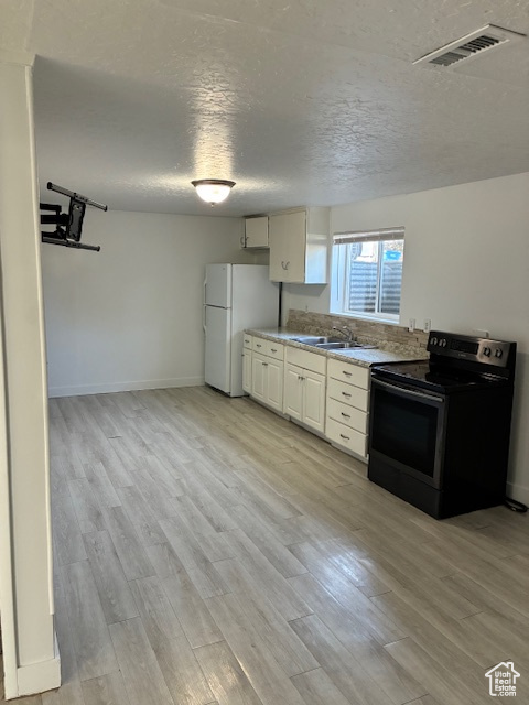 Kitchen featuring range with electric stovetop, freestanding refrigerator, light wood-style flooring, a textured ceiling, and white cabinetry