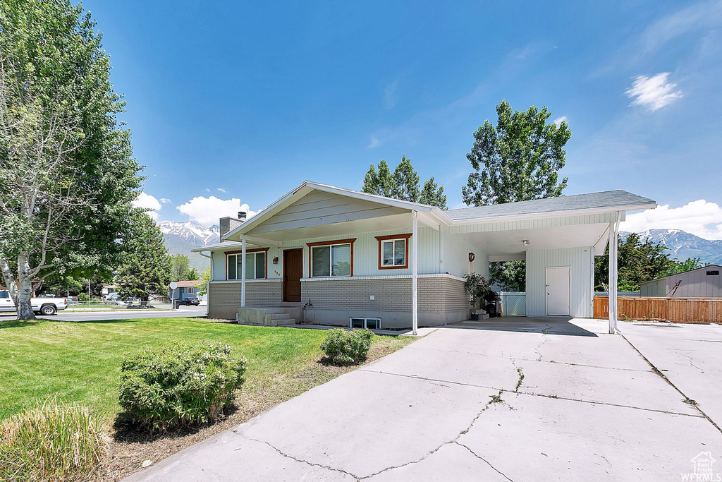 View of front of house with concrete driveway, an attached carport, a mountain view, a chimney, and covered porch