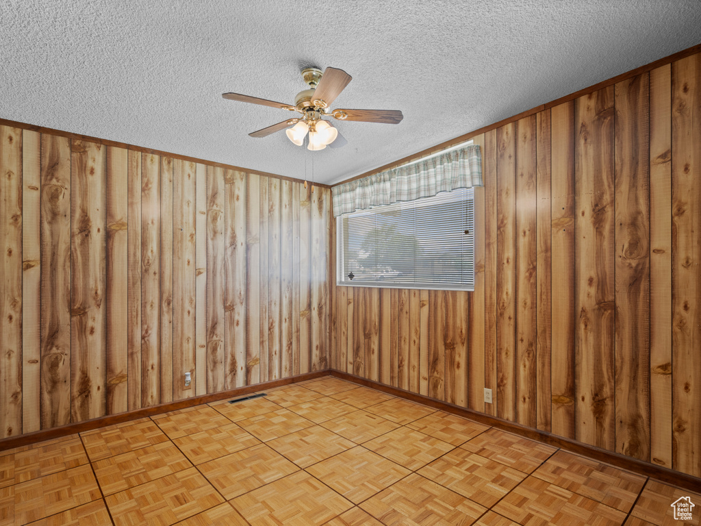 Spare room featuring a ceiling fan, wood walls, and a textured ceiling