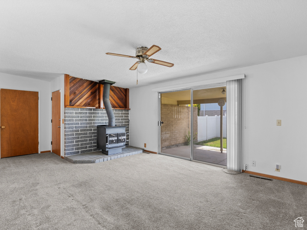 Unfurnished living room with a wood stove, ceiling fan, carpet, and a textured ceiling