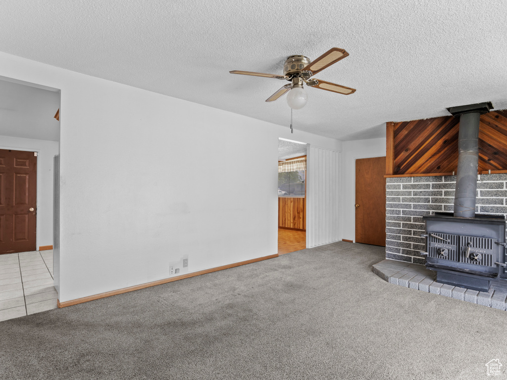 Unfurnished living room with a wood stove, a ceiling fan, carpet, and a textured ceiling