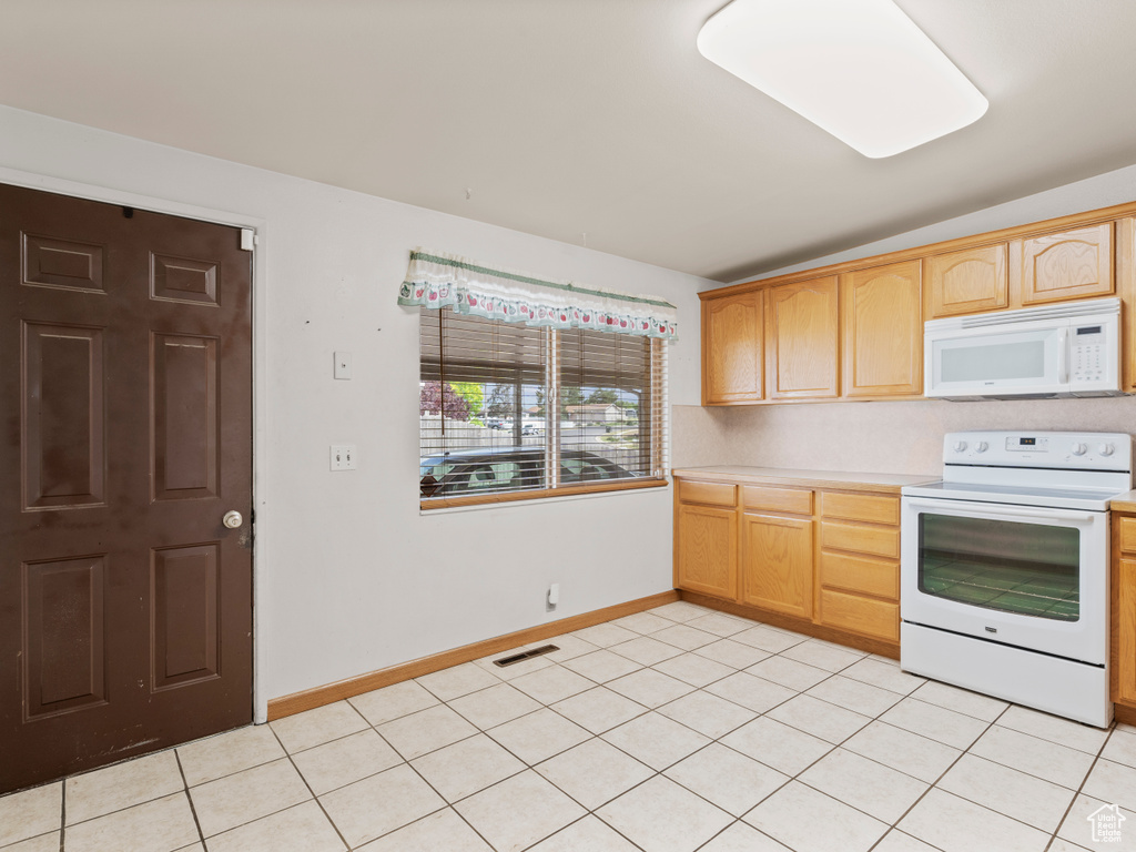 Kitchen featuring white appliances, light countertops, light tile patterned floors, and light brown cabinets