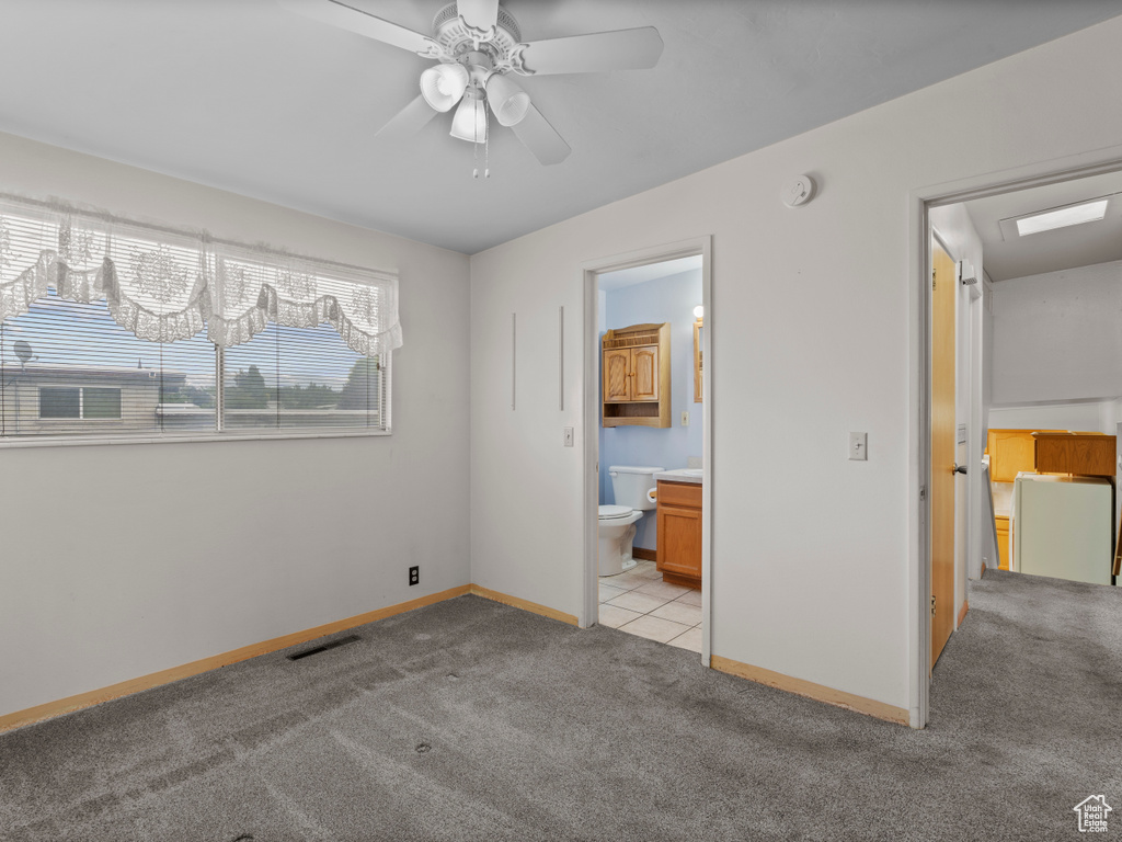 Unfurnished bedroom featuring light carpet, ensuite bathroom, and ceiling fan