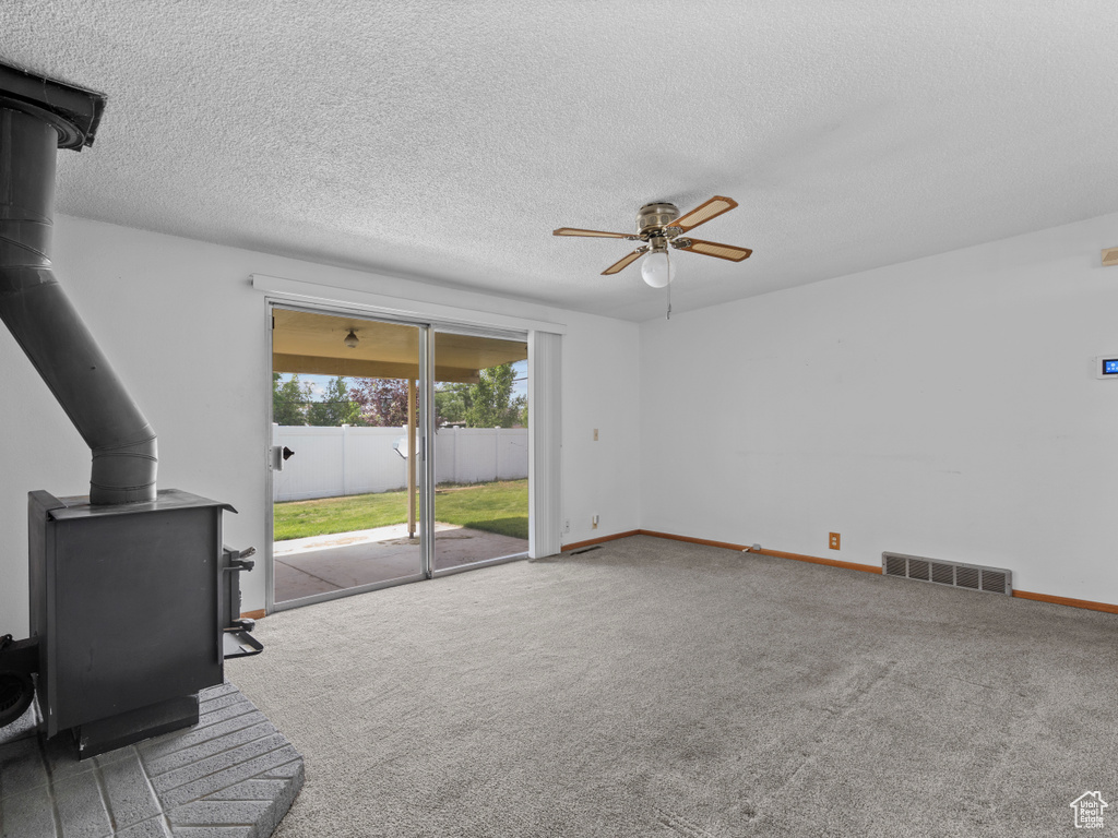 Unfurnished living room featuring a wood stove, a ceiling fan, carpet, and a textured ceiling