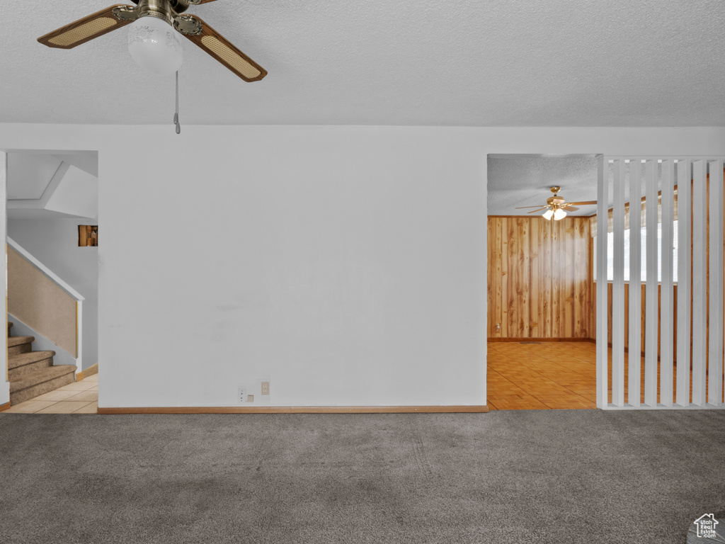 Spare room with ceiling fan, carpet, wood walls, a textured ceiling, and stairs