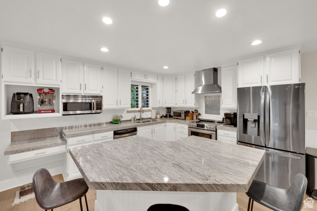 Kitchen featuring wall chimney range hood, stainless steel appliances, a breakfast bar, tasteful backsplash, and white cabinets