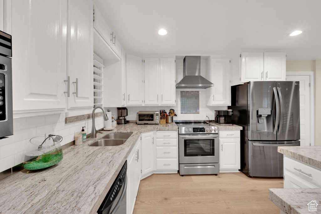 Kitchen featuring wall chimney exhaust hood, appliances with stainless steel finishes, tasteful backsplash, white cabinetry, and recessed lighting