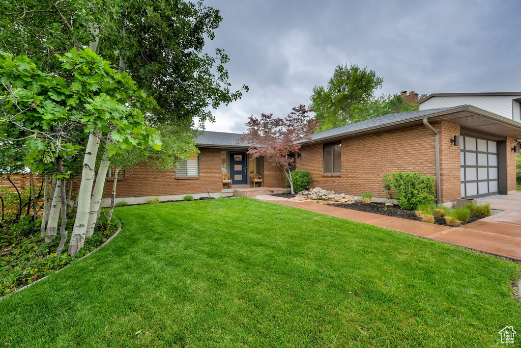 View of front facade featuring brick siding, a front lawn, a garage, and a chimney