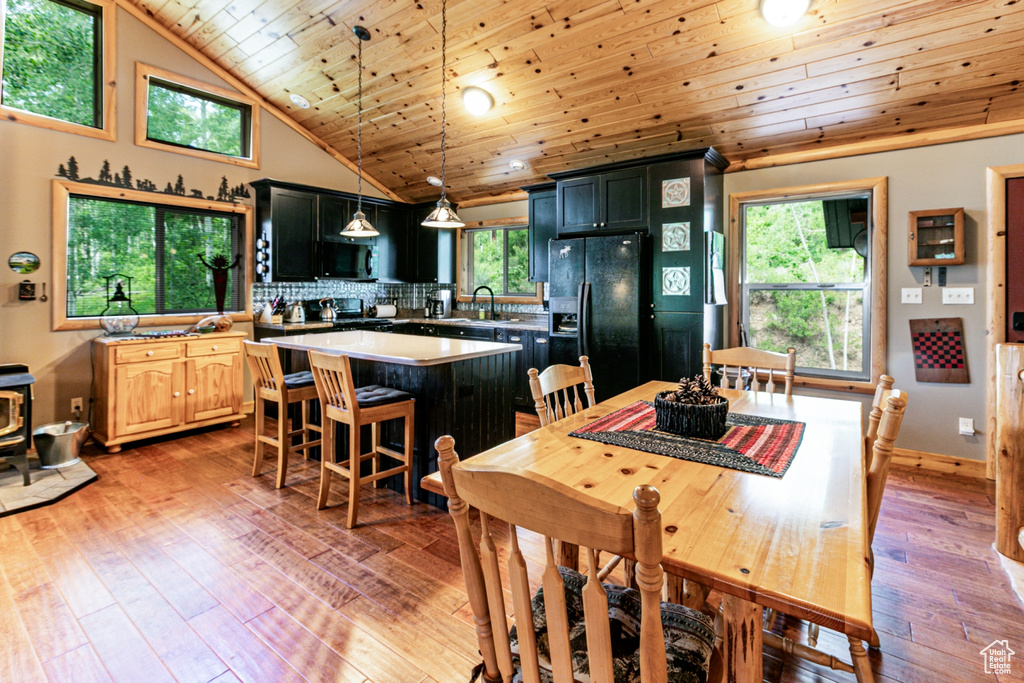 Dining room with wooden ceiling, light wood finished floors, plenty of natural light, high vaulted ceiling, and a wood stove