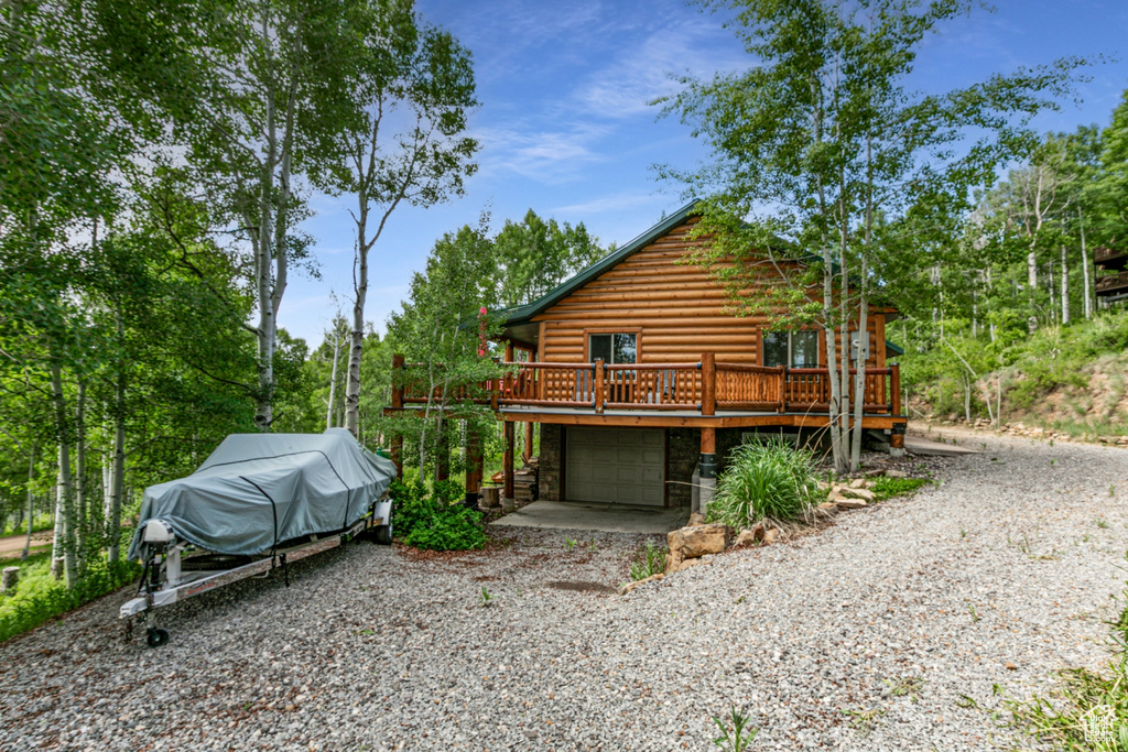 View of property exterior featuring a deck, gravel driveway, stone siding, log exterior, and a garage