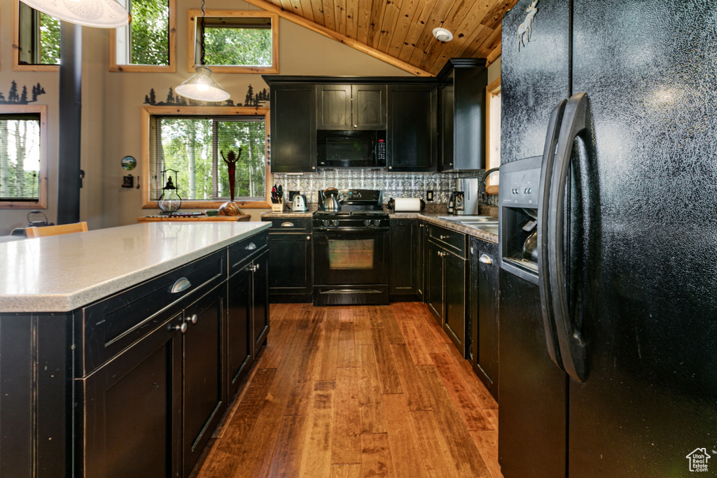 Kitchen with black appliances, dark cabinets, hardwood / wood-style floors, vaulted ceiling, and decorative backsplash