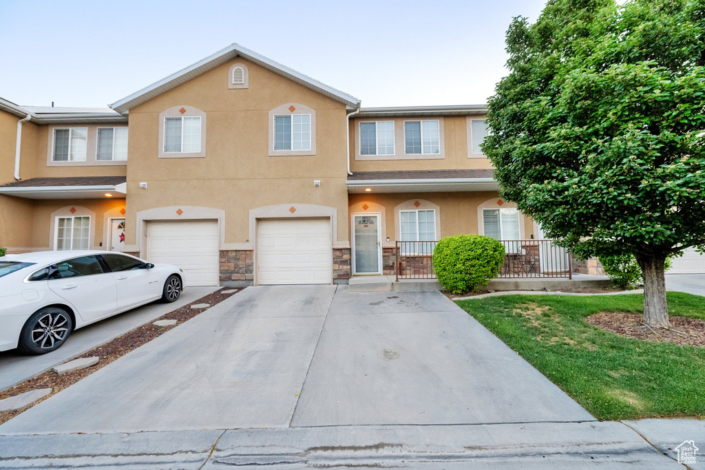 View of property featuring driveway, an attached garage, stucco siding, and stone siding