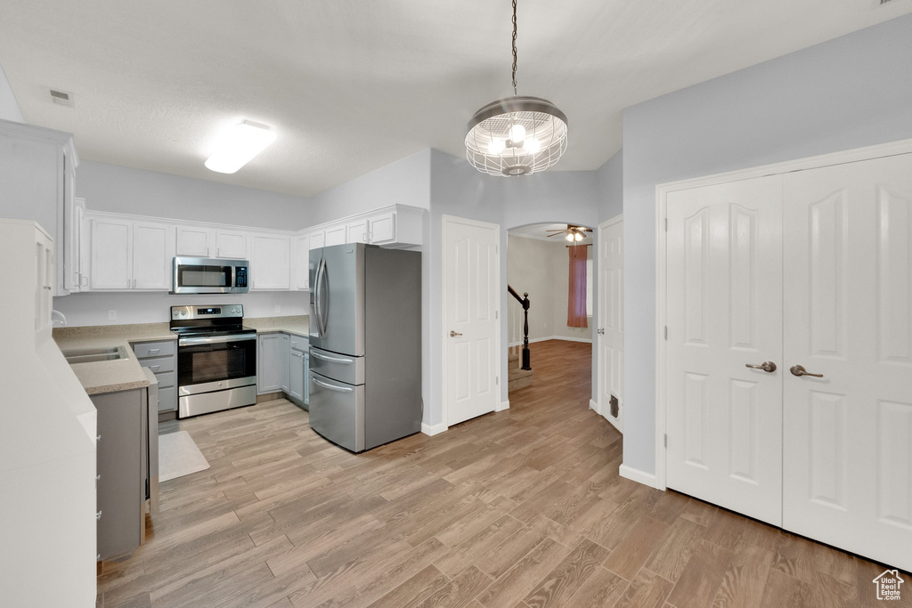 Kitchen with appliances with stainless steel finishes, light countertops, white cabinets, light wood-style floors, and decorative light fixtures