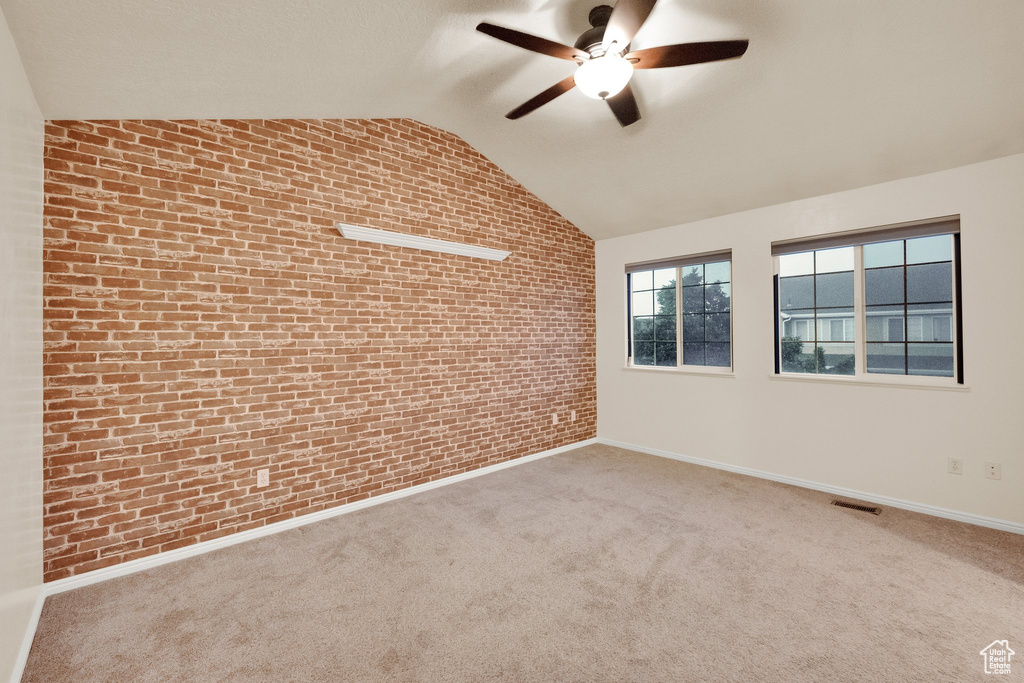 Carpeted empty room featuring brick wall, a ceiling fan, and lofted ceiling