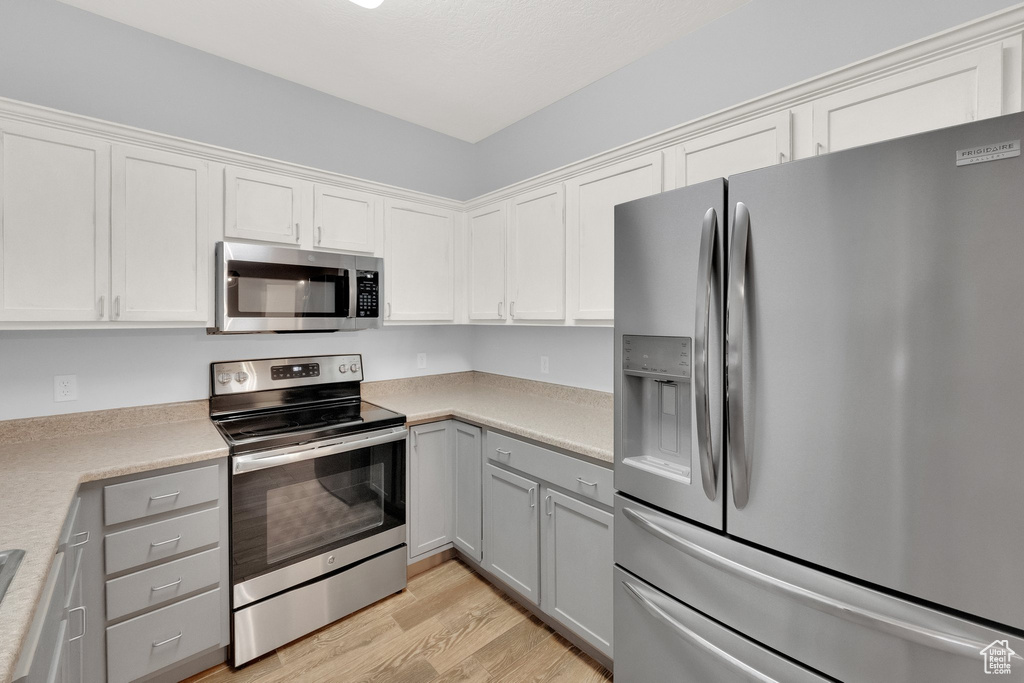 Kitchen featuring appliances with stainless steel finishes, light wood finished floors, light countertops, gray cabinetry, and white cabinets