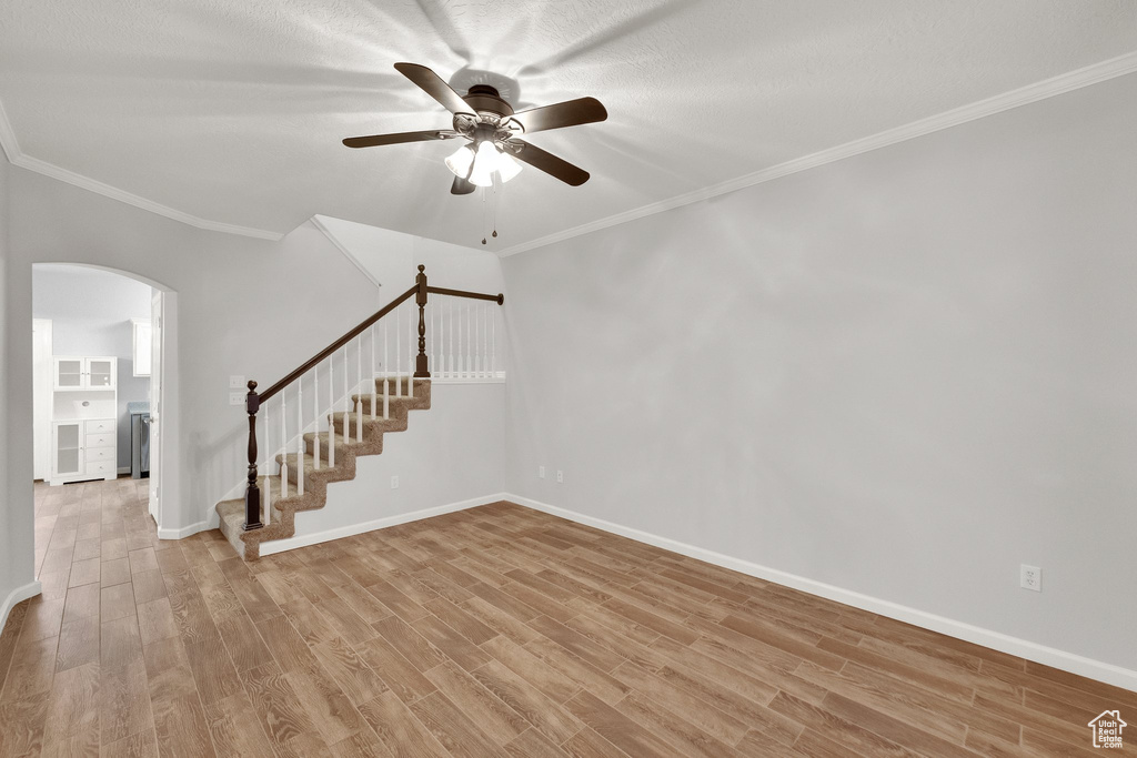 Unfurnished room featuring arched walkways, light wood-style flooring, stairs, a ceiling fan, and crown molding