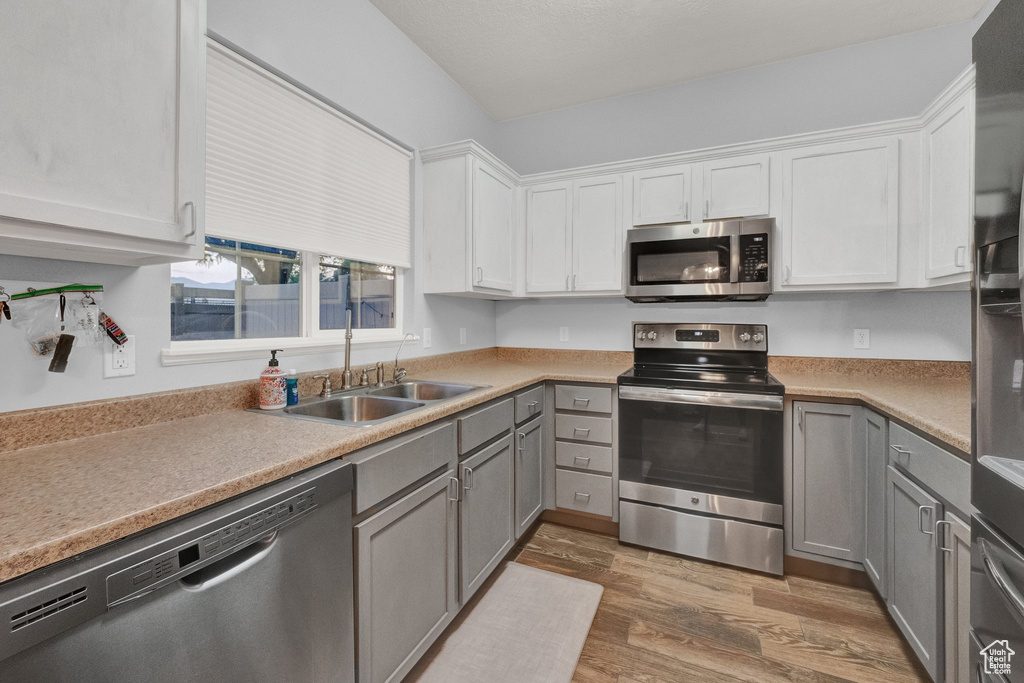 Kitchen with stainless steel appliances, light wood-style flooring, gray cabinetry, and white cabinetry