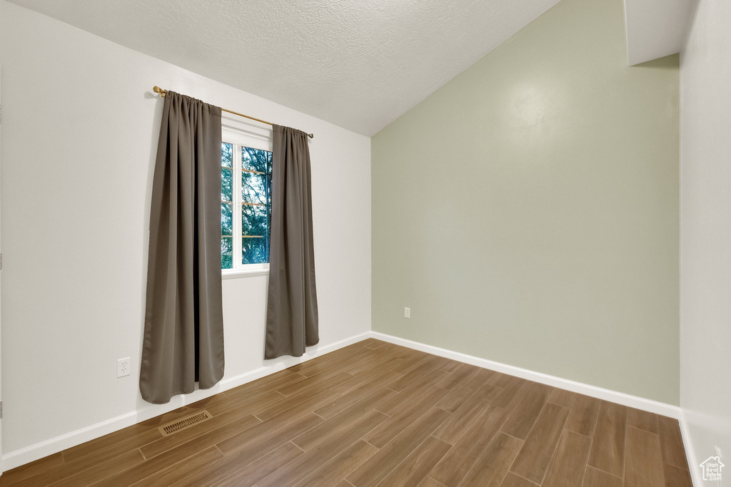 Spare room featuring wood finished floors, lofted ceiling, and a textured ceiling