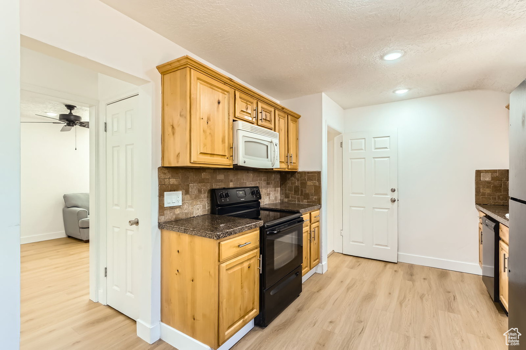 Kitchen featuring black appliances, light wood-style floors, decorative backsplash, dark countertops, and a textured ceiling