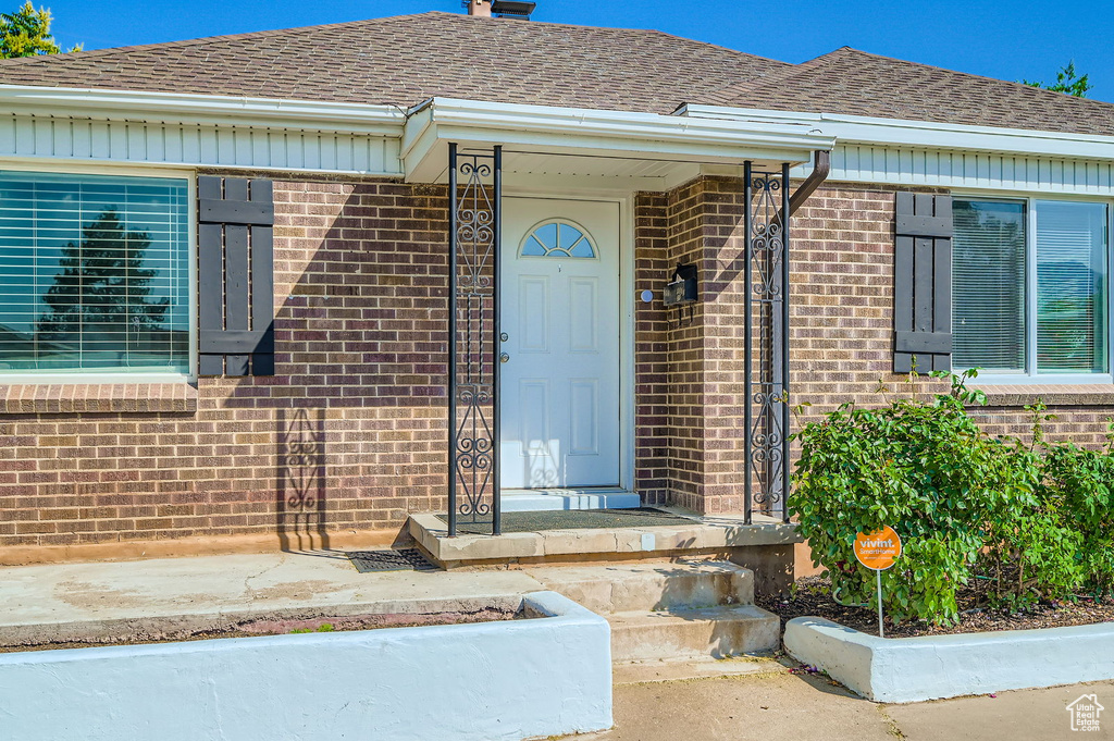 Entrance to property with brick siding, roof with shingles, and a chimney