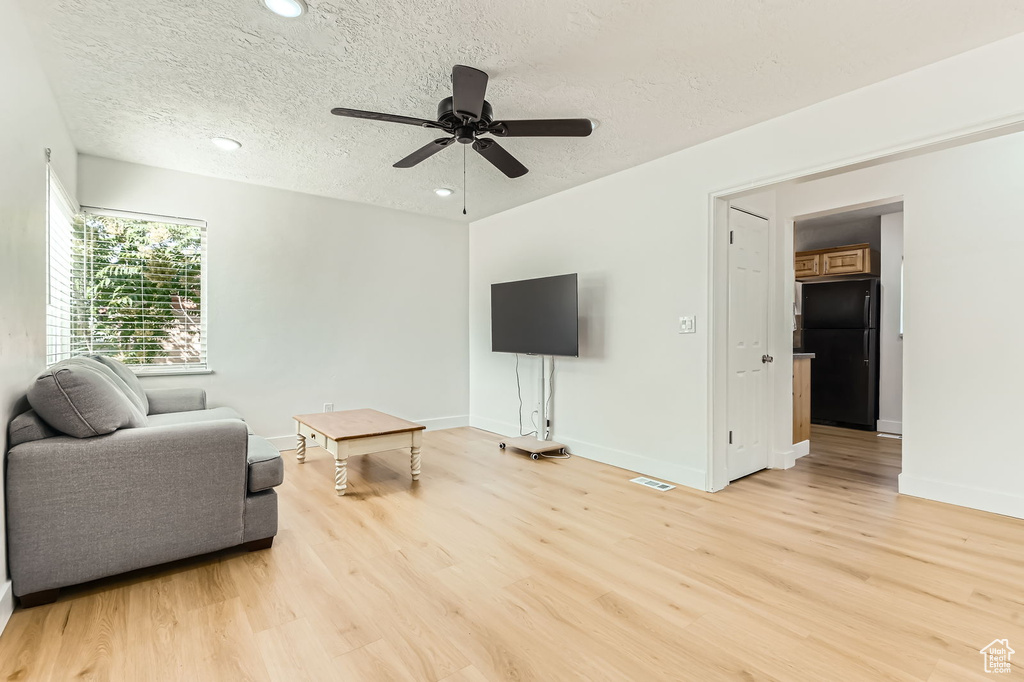 Living room featuring light wood-type flooring, a textured ceiling, a ceiling fan, and recessed lighting
