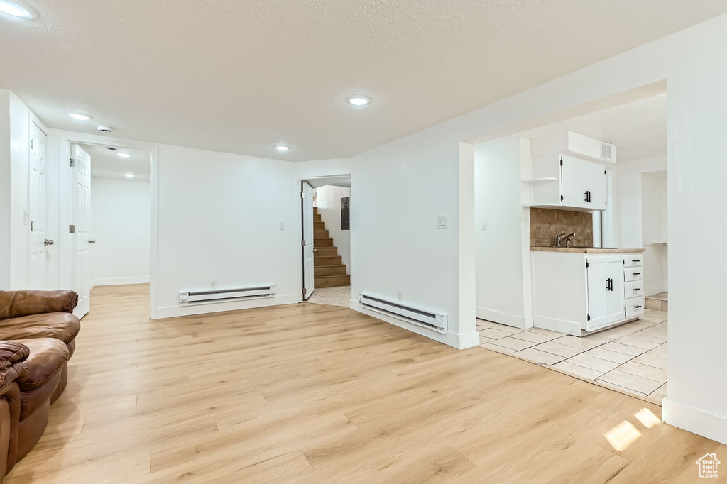 Living area with a baseboard radiator, stairway, light wood-style floors, and recessed lighting