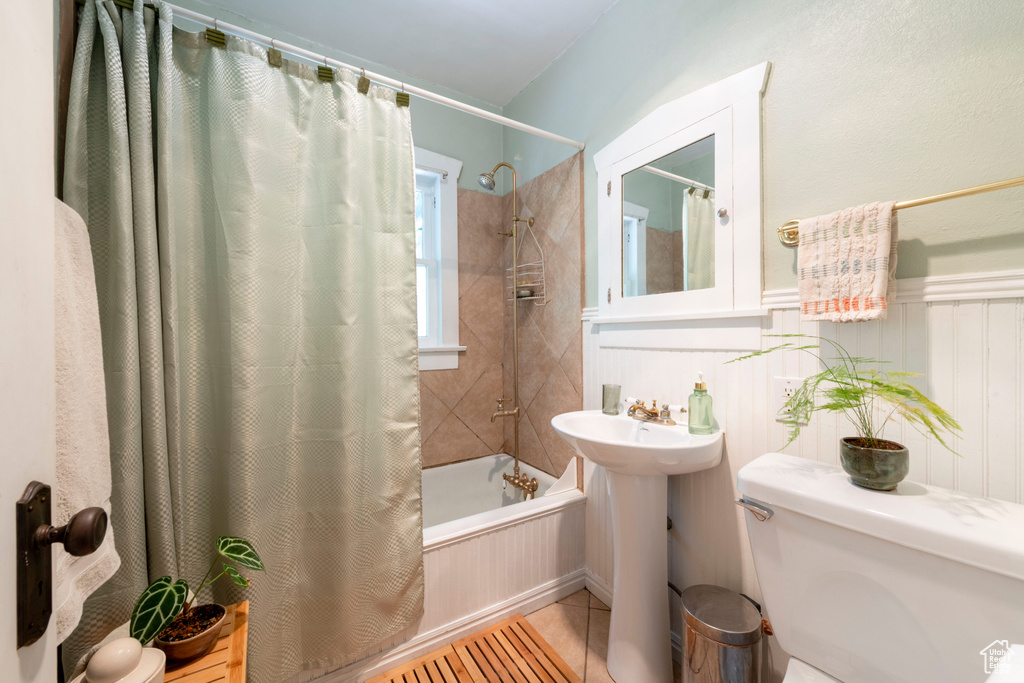 Bathroom featuring shower / bath combo with shower curtain, tile patterned floors, and a wainscoted wall
