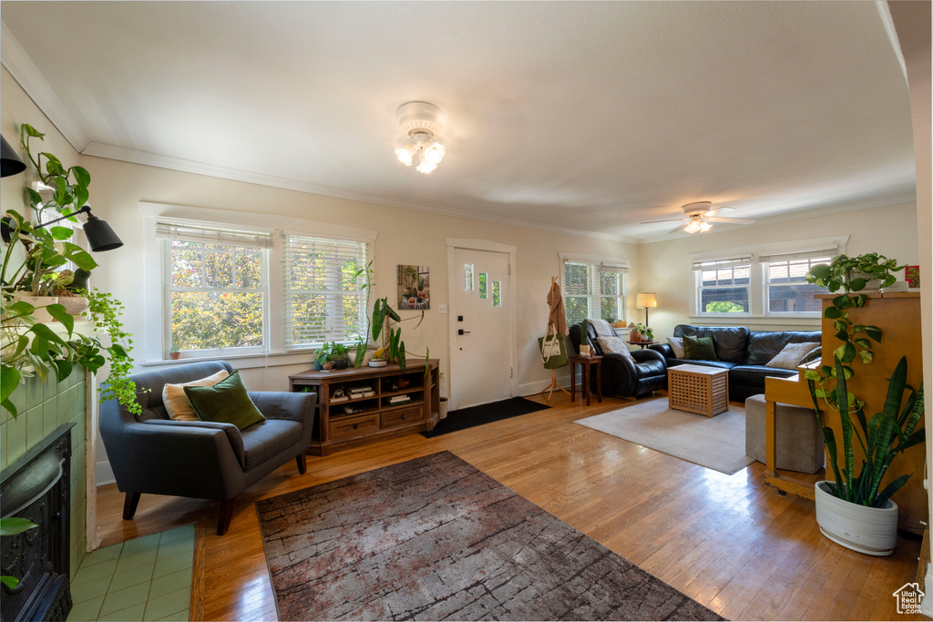 Living area with wood finished floors, a tiled fireplace, crown molding, and ceiling fan