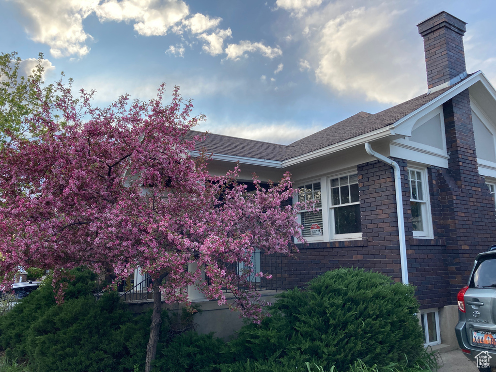 View of side of home with a chimney, a shingled roof, and brick siding