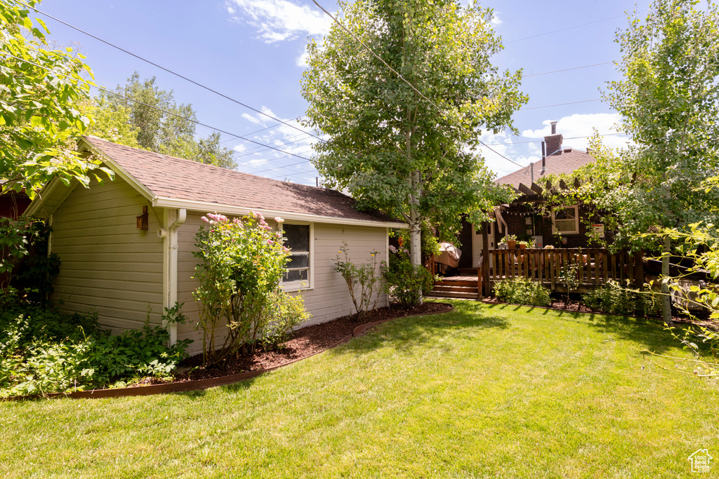 View of green lawn with a wooden deck and an outdoor structure