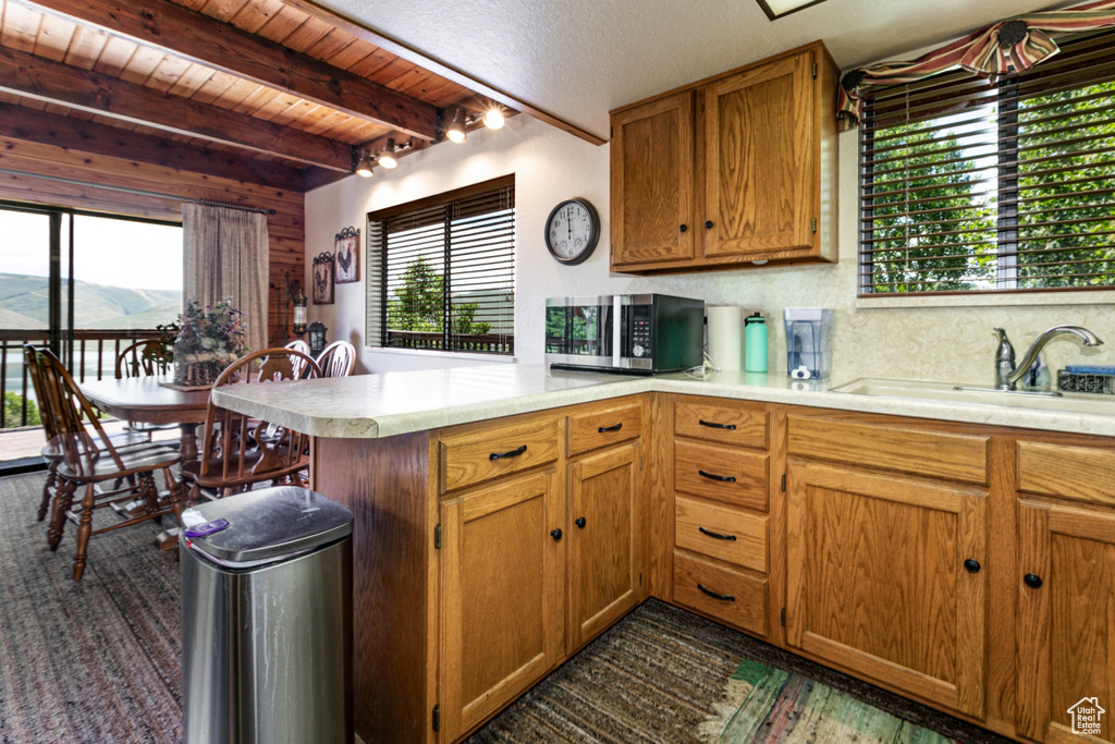 Kitchen with stainless steel microwave, a peninsula, light countertops, plenty of natural light, and a wooden ceiling with exposed beams