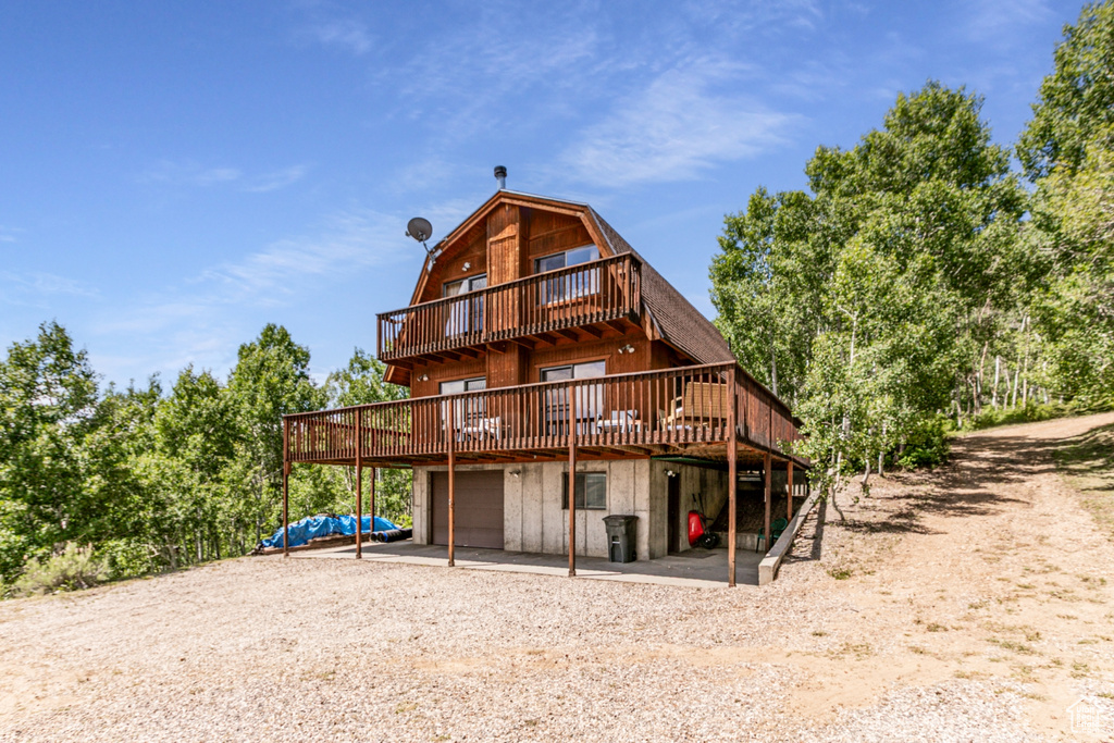 Back of property with a gambrel roof, a garage, a deck, and dirt driveway