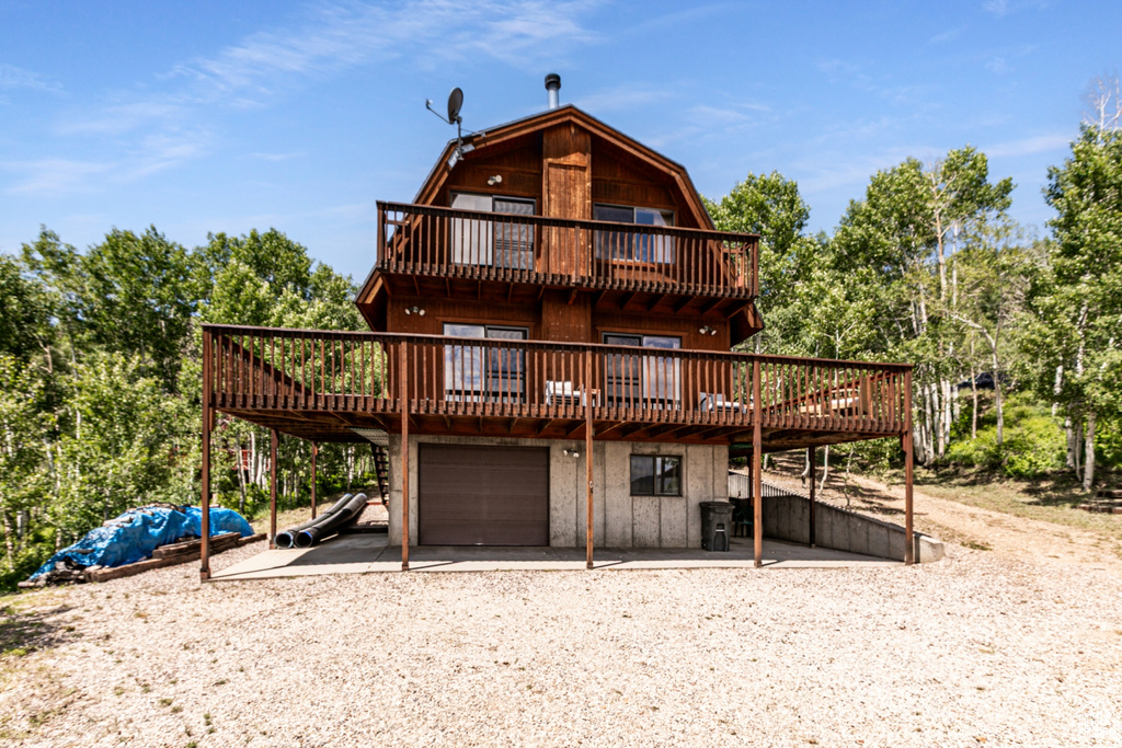 View of front of home featuring a garage, a gambrel roof, dirt driveway, and a wooden deck