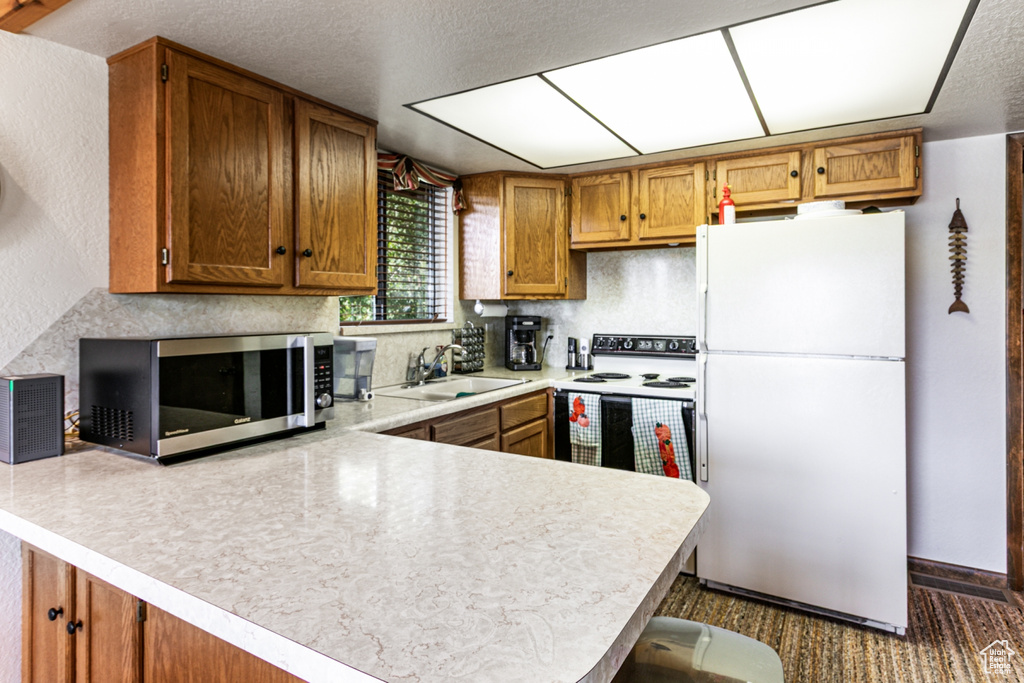 Kitchen with white appliances, a peninsula, light countertops, brown cabinetry, and a textured ceiling