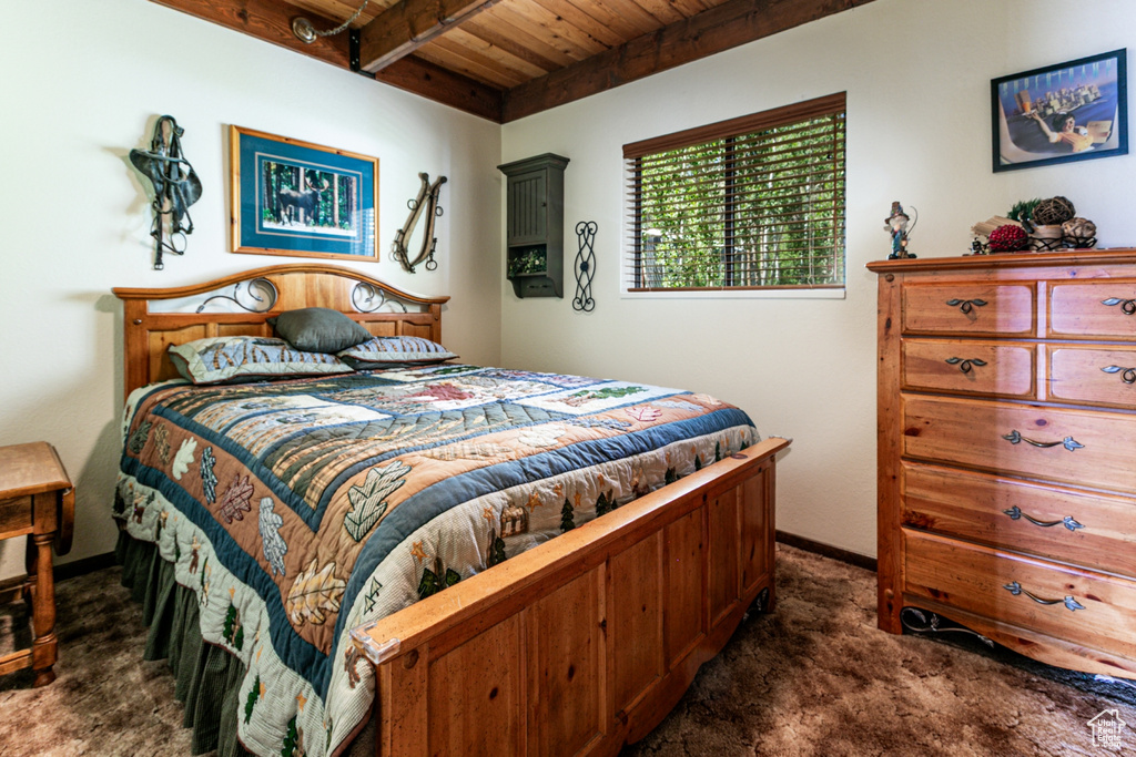 Bedroom with dark colored carpet and a wooden ceiling with exposed beams