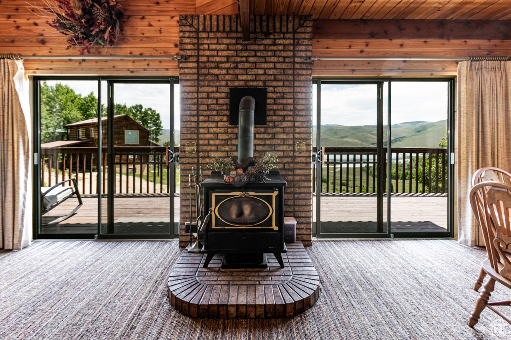 Carpeted living area featuring wood walls, a wood stove, plenty of natural light, wooden ceiling, and a mountain view