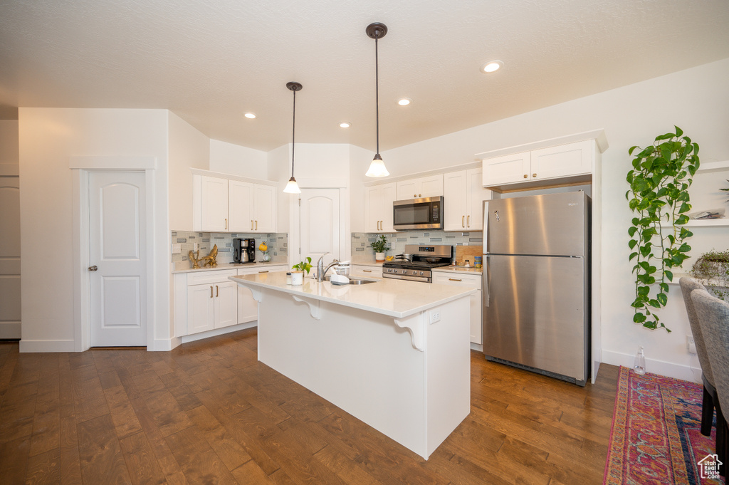 Kitchen featuring stainless steel appliances, backsplash, light countertops, a kitchen bar, and white cabinets