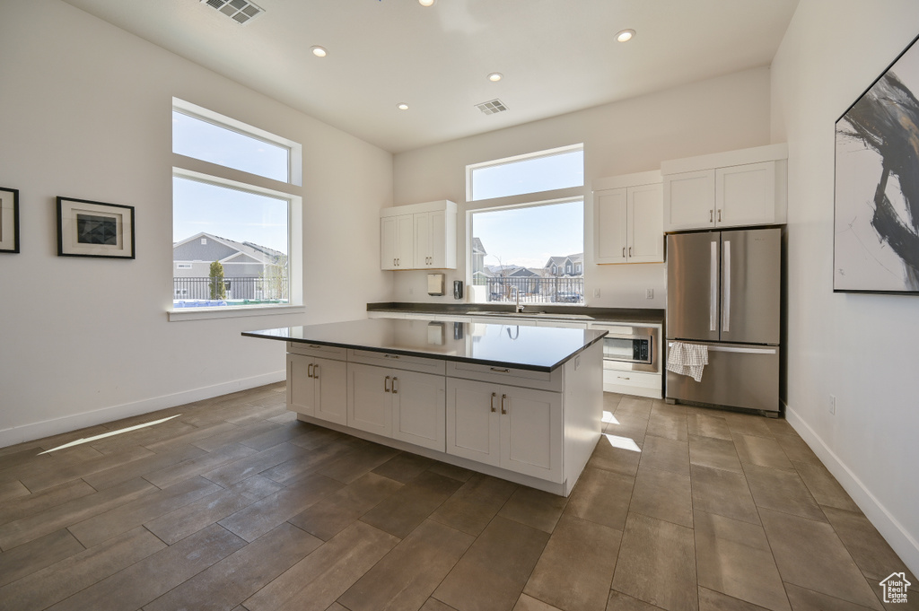 Kitchen featuring stainless steel appliances, white cabinetry, a center island, recessed lighting, and dark countertops