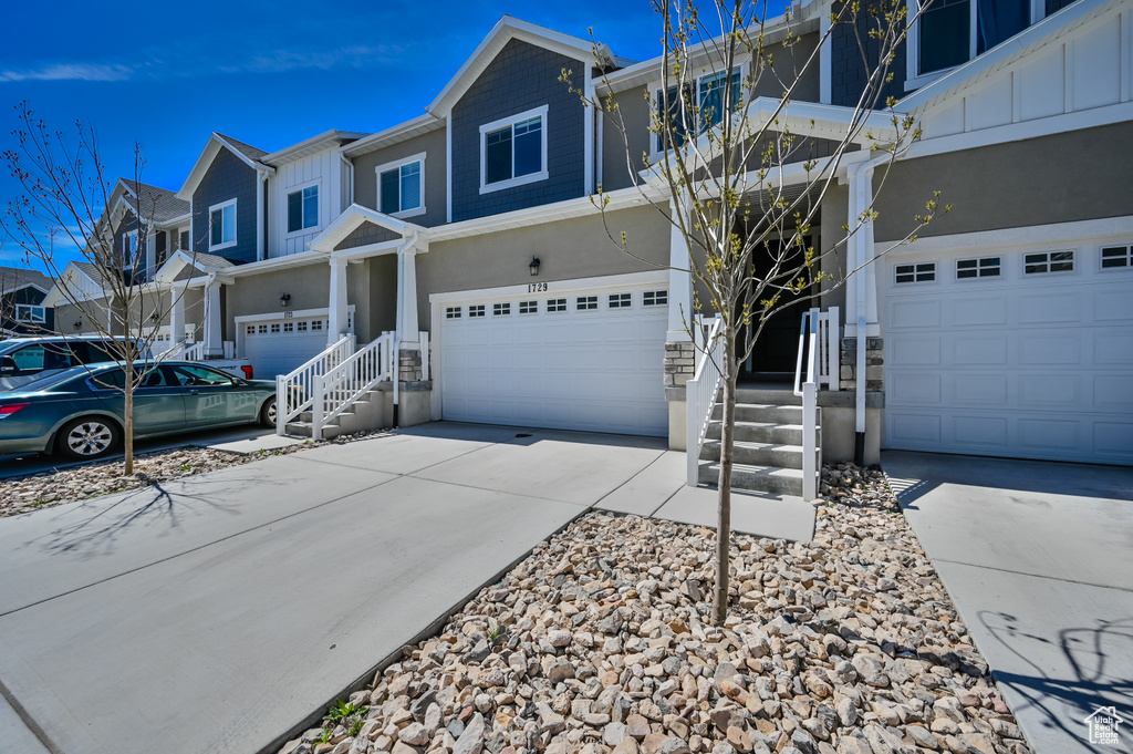 View of front of property with an attached garage, concrete driveway, stucco siding, a residential view, and board and batten siding