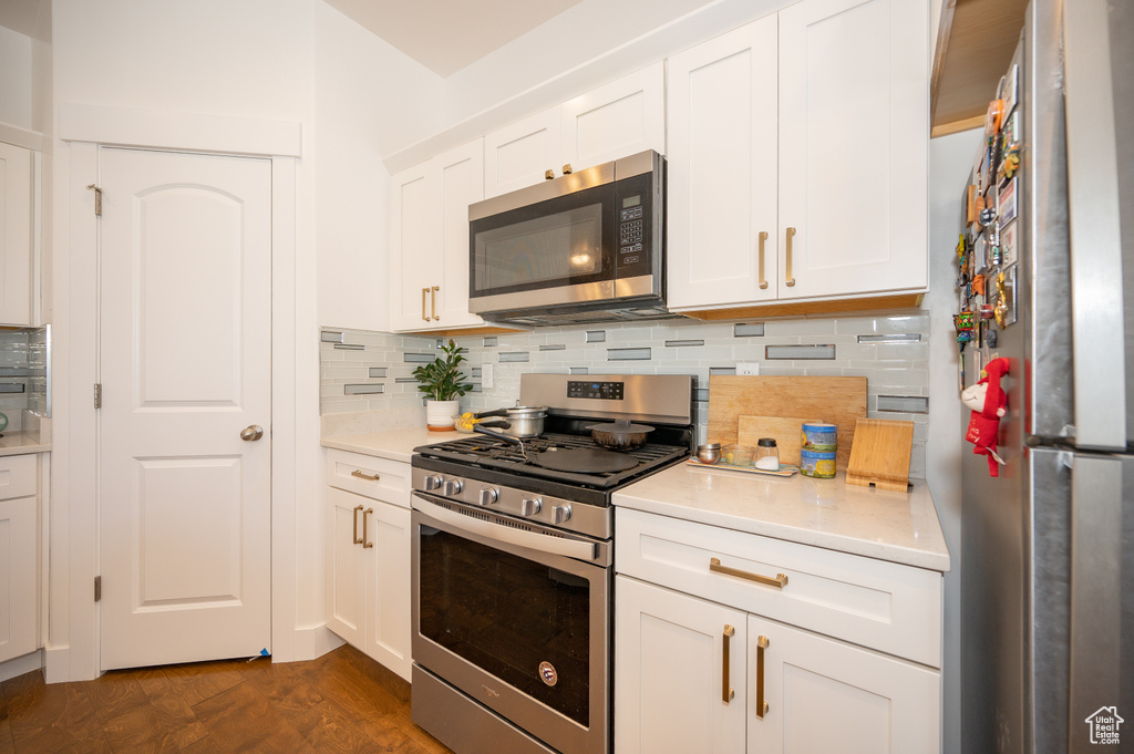 Kitchen featuring stainless steel appliances, light countertops, backsplash, and white cabinetry