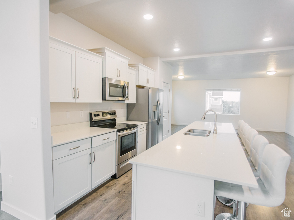 Kitchen with stainless steel appliances, a breakfast bar, light wood-type flooring, a kitchen island with sink, and white cabinetry