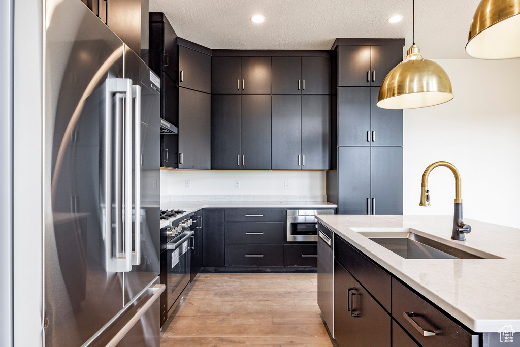 Kitchen featuring stainless steel appliances, pendant lighting, light wood-style floors, light stone counters, and recessed lighting