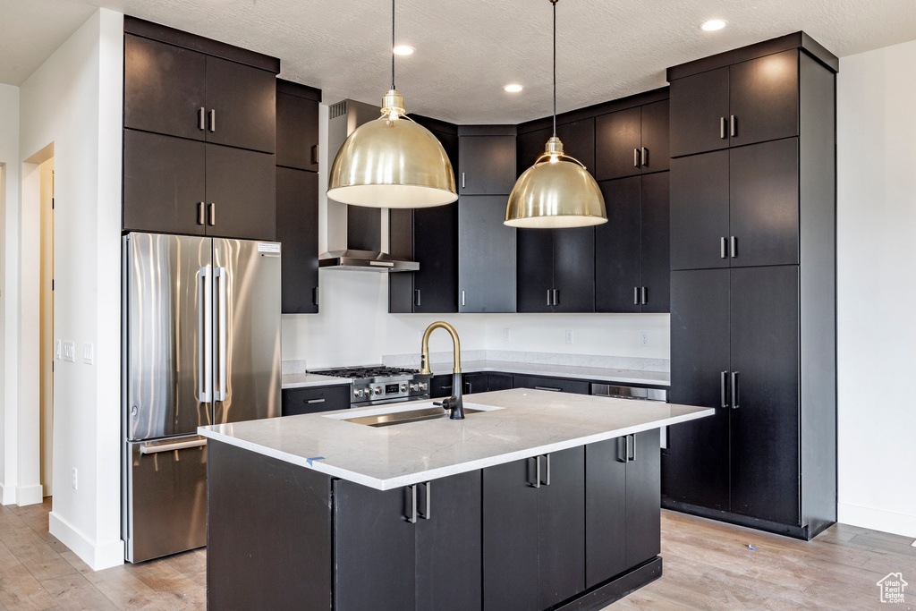 Kitchen with high end refrigerator, light wood finished floors, decorative light fixtures, a center island with sink, and a kitchen bar