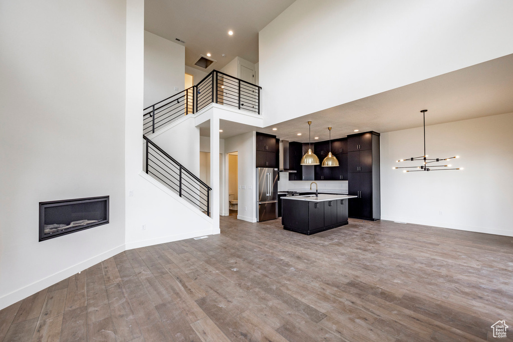 Unfurnished living room featuring stairs, a towering ceiling, a chandelier, wood finished floors, and recessed lighting